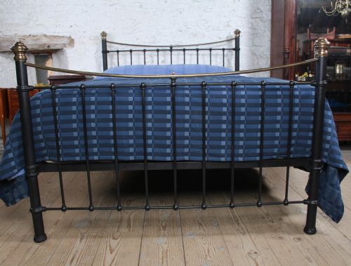 fig 2. An Edwardian black iron and brass king-size bedstead featuring a curved dip rail and brass corner finials.