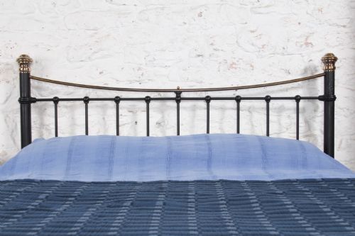 fig 4. An Edwardian black iron and brass king-size bedstead featuring a curved dip rail and brass corner finials.