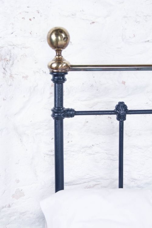 fig 3. A Victorian double bed frame featuring a dark cast iron headboard with vertical spindles and a polished brass top rail with corner finials.