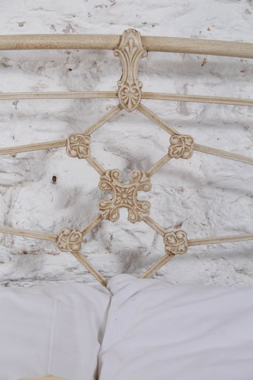 fig 4. A cream-painted Victorian metal double bed frame featuring a arched wrought iron headboard with decorative cast iron joints.