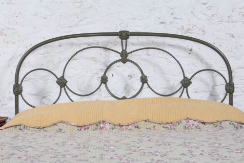 fig 2. Victorian dark green cast iron double bedstead featuring an arched headboard with decorative scrollwork and a low foot end.
