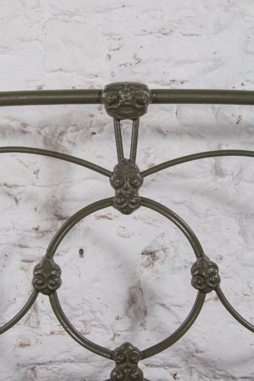 fig 4. Victorian dark green cast iron double bedstead featuring an arched headboard with decorative scrollwork and a low foot end.