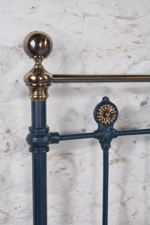 fig 3. A Victorian king size cast iron bedstead with brass top rail and decorative rosettes, dressed in white and dark blue bedding.