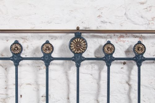 fig 4. A Victorian king size cast iron bedstead with brass top rail and decorative rosettes, dressed in white and dark blue bedding.