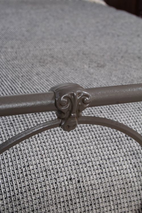 fig 1. An antique dark grey iron bed frame featuring decorative curved tubing and cast detailing dressed with a textured grey blanket.