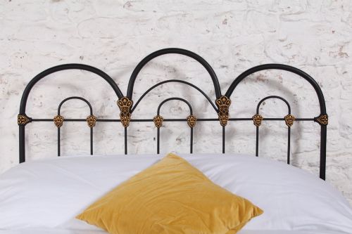 fig 2. A black Victorian cast iron double bedstead featuring triple arched headboard metalwork with brass castings and a low foot end.