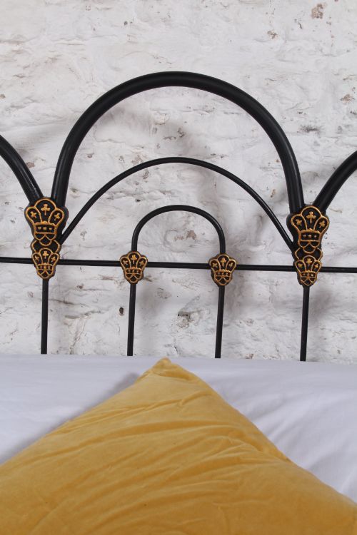 fig 3. A black Victorian cast iron double bedstead featuring triple arched headboard metalwork with brass castings and a low foot end.