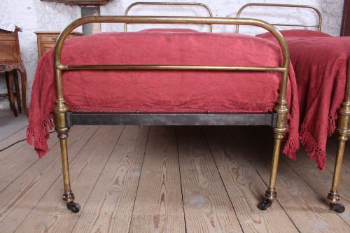 fig 2. A pair of antique tubular brass single bed frames featuring rounded headboards, simple footboards, turned leg details, and brass castors.