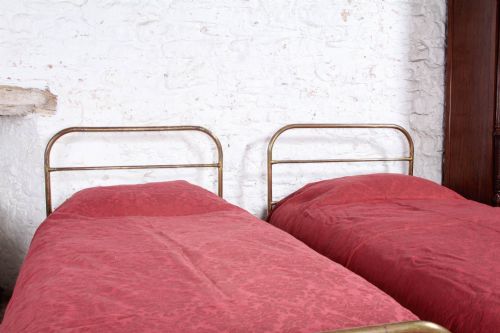 fig 4. A pair of antique tubular brass single bed frames featuring rounded headboards, simple footboards, turned leg details, and brass castors.