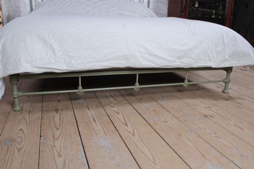 fig 1. A super king French iron bedstead featuring a sage green painted frame, vertical iron spindles, brass top rails, and brass oval motifs.