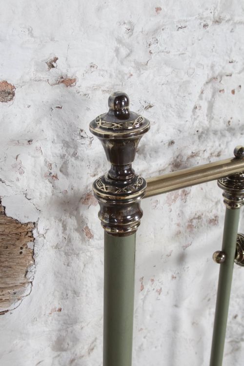 fig 3. A super king French iron bedstead featuring a sage green painted frame, vertical iron spindles, brass top rails, and brass oval motifs.