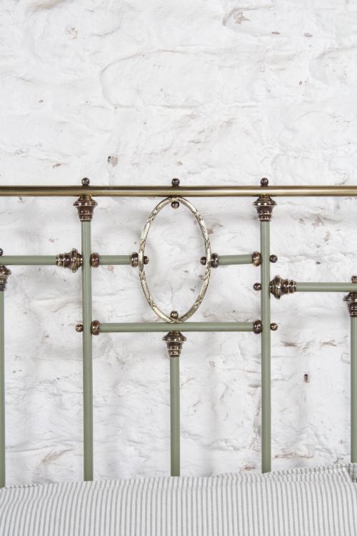fig 4. A super king French iron bedstead featuring a sage green painted frame, vertical iron spindles, brass top rails, and brass oval motifs.