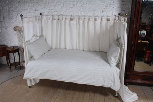 fig 4. A painted single iron four-poster bed frame featuring decorative central scrollwork, brass top finials, and lightweight drapery.