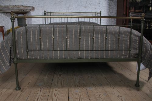 fig 2. A dark green painted iron and brass king-size bedstead featuring vertical iron spindles and polished brass top rails.