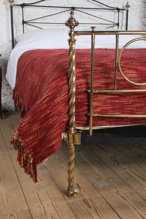 fig 4. A Victorian iron and brass king-size bedstead featuring barley twist posts, ornate brass scrollwork on the footboard, and a arched black iron headboard.