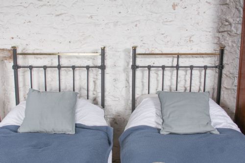 fig 2. A pair of Edwardian black iron single beds featuring square tube framing, vertical spindles, and polished brass top rails.