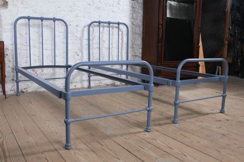 fig 1. A pair of slate blue painted tubular iron single bed frames positioned side by side on a light wooden floor.