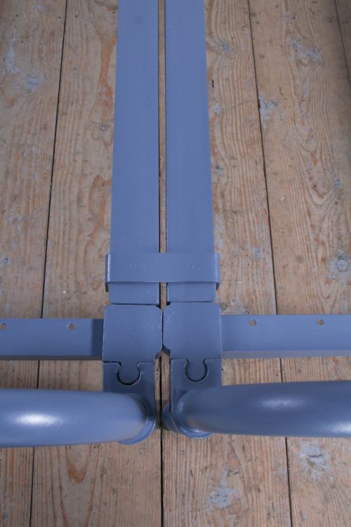 fig 3. A pair of slate blue painted tubular iron single bed frames positioned side by side on a light wooden floor.