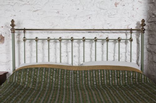 fig 1. A sage green painted iron super king bedstead featuring vertical spindles, a polished brass top rail, brass decorative finials, and a low foot end.