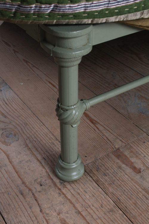 fig 2. A sage green painted iron super king bedstead featuring vertical spindles, a polished brass top rail, brass decorative finials, and a low foot end.