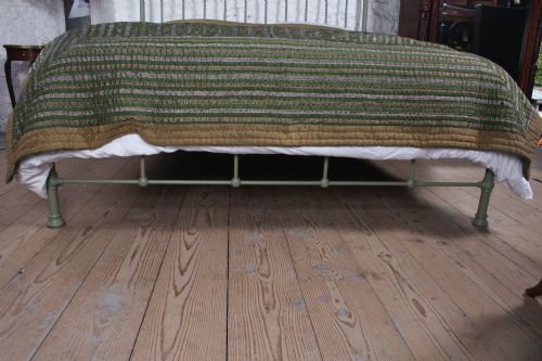 fig 3. A sage green painted iron super king bedstead featuring vertical spindles, a polished brass top rail, brass decorative finials, and a low foot end.