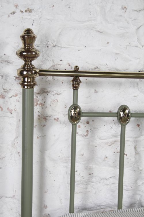 fig 4. A sage green painted iron super king bedstead featuring vertical spindles, a polished brass top rail, brass decorative finials, and a low foot end.