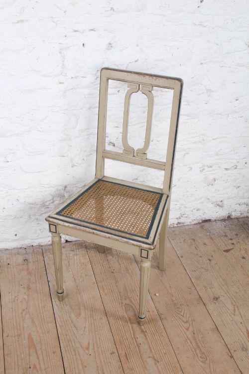 fig 1. A beige painted French side chair featuring a woven cane seat, fluted tapered legs, and an open geometric back motif outlined with dark paint.