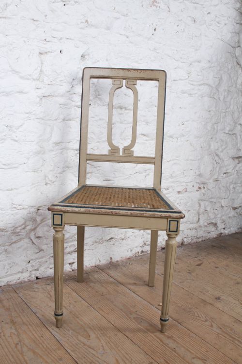 fig 2. A beige painted French side chair featuring a woven cane seat, fluted tapered legs, and an open geometric back motif outlined with dark paint.