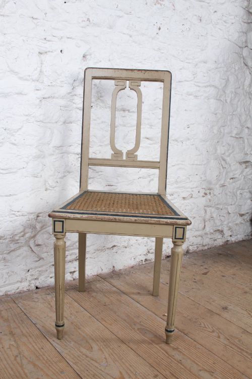 fig 3. A beige painted French side chair featuring a woven cane seat, fluted tapered legs, and an open geometric back motif outlined with dark paint.