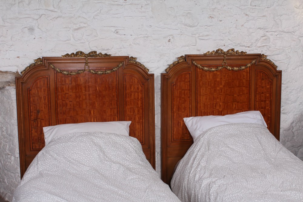 A pair of antique French fruitwood single beds featuring geometric parquetry inlay and decorative gilt bronze mounts on the headboards and footboards. View II
