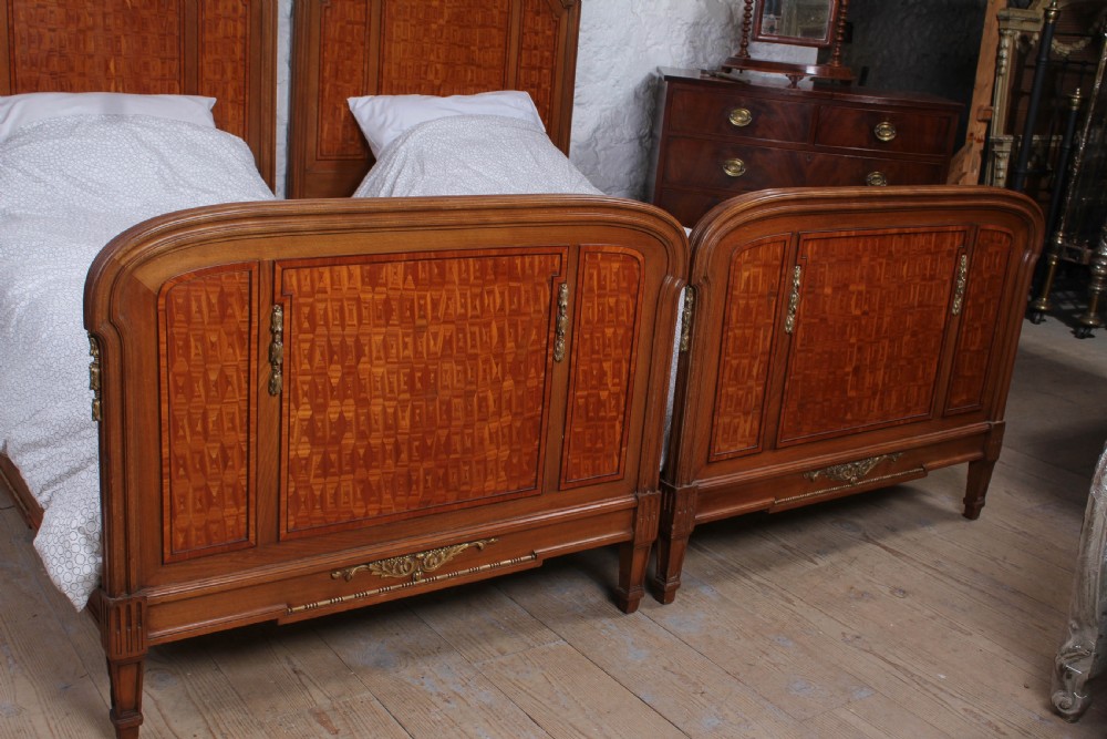 A pair of antique French fruitwood single beds featuring geometric parquetry inlay and decorative gilt bronze mounts on the headboards and footboards. View IV