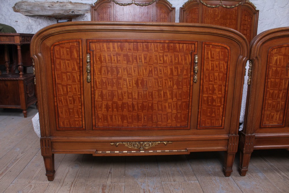A pair of antique French fruitwood single beds featuring geometric parquetry inlay and decorative gilt bronze mounts on the headboards and footboards. View V