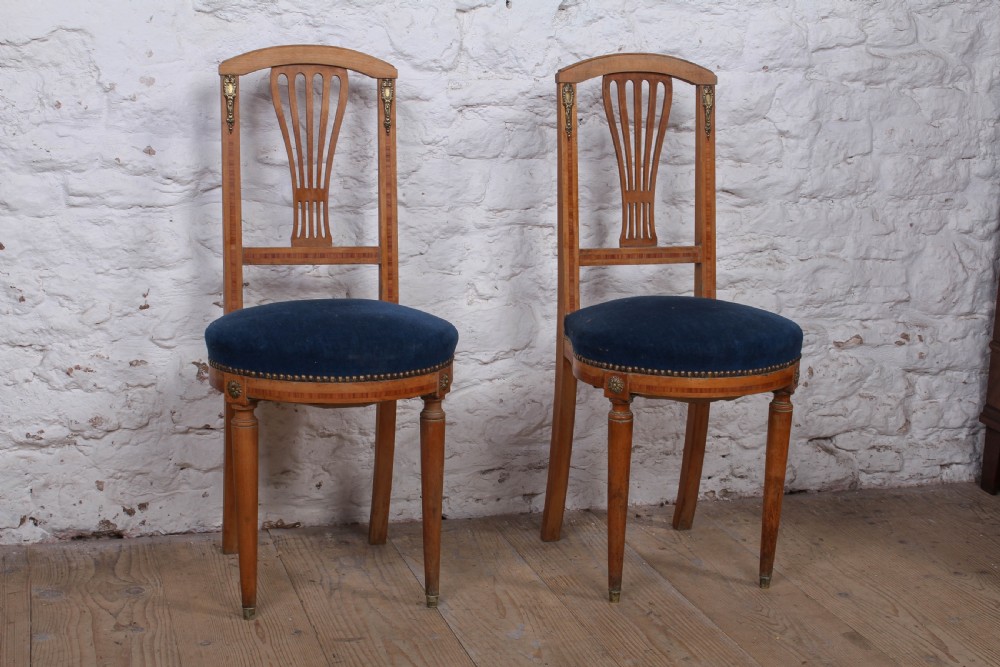 A pair of French Louis XVI style side chairs with inlaid light wood frames, pierced balloon back splats, and circular navy blue velvet upholstered seats.