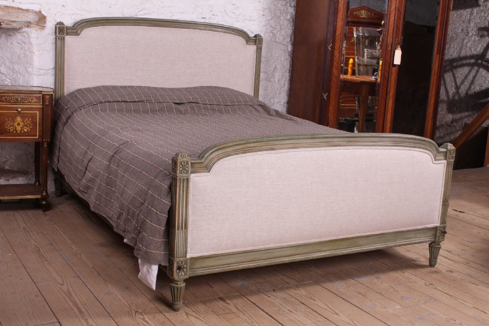 A Louis XVI style French king-size bed frame featuring a muted green painted wooden trim, fluted corner posts, rosettes, and cream linen upholstered panels on the headboard and footboard.