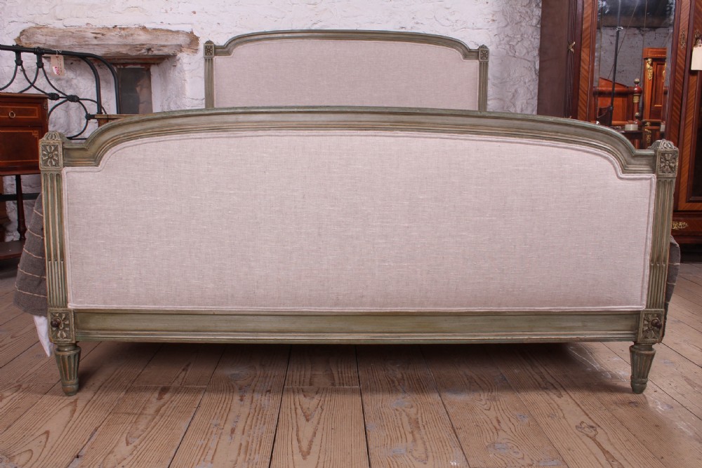 A Louis XVI style French king-size bed frame featuring a muted green painted wooden trim, fluted corner posts, rosettes, and cream linen upholstered panels on the headboard and footboard. View II