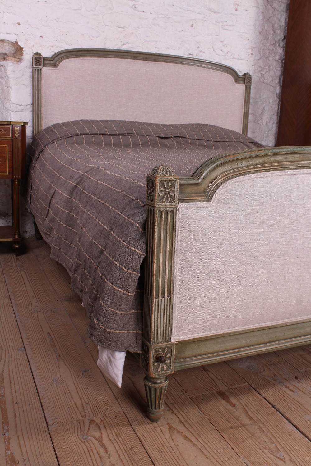 A Louis XVI style French king-size bed frame featuring a muted green painted wooden trim, fluted corner posts, rosettes, and cream linen upholstered panels on the headboard and footboard. View IV