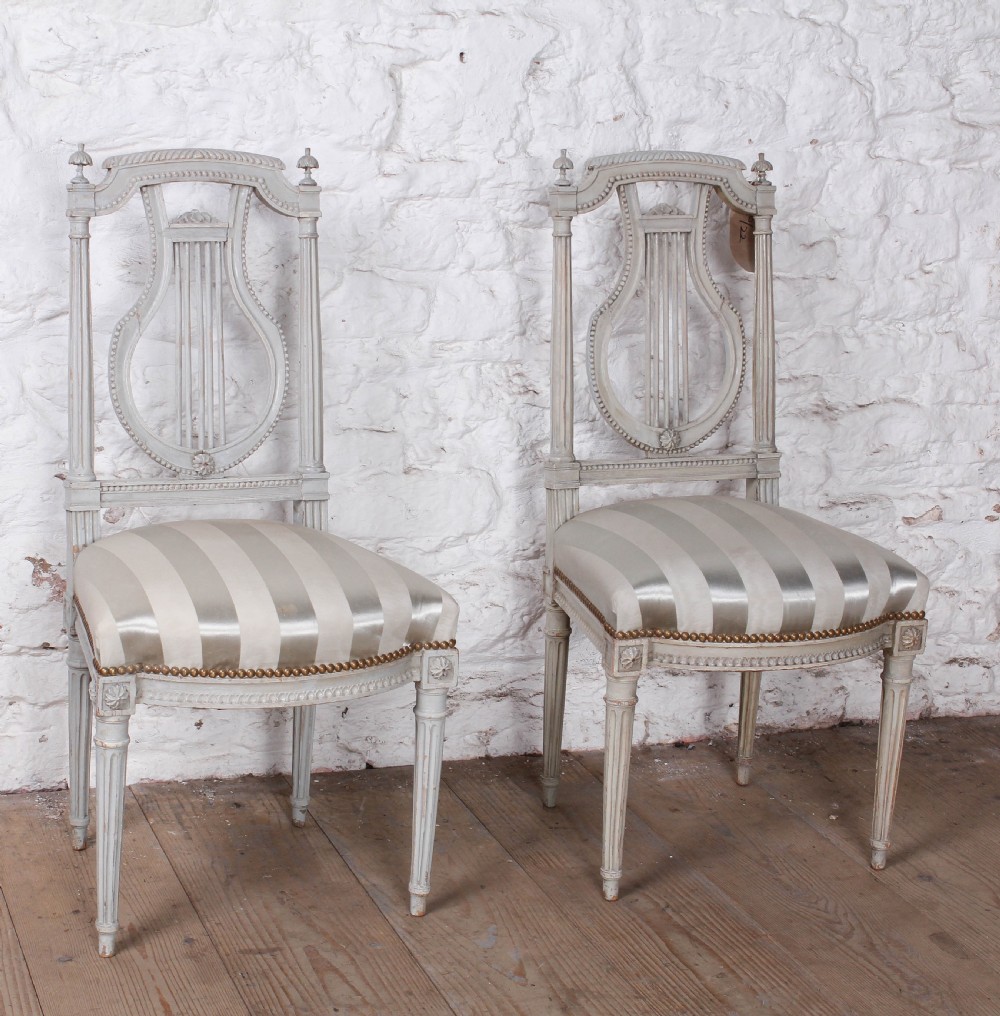A pair of light grey painted French side chairs featuring lyre-shaped backrests, fluted tapered legs, and cream striped satin upholstery.
