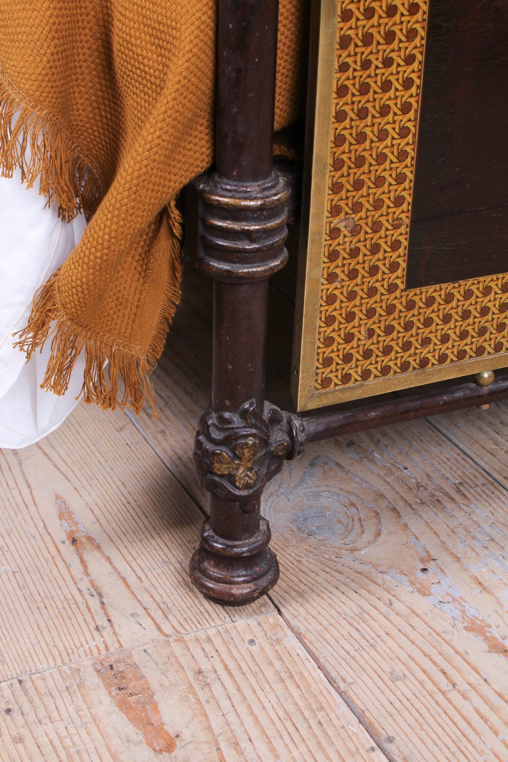 An antique European double bed featuring a dark iron frame, brass top rails, vertical spindles on the headboard, and decorative painted panel inserts on the footboard. View V