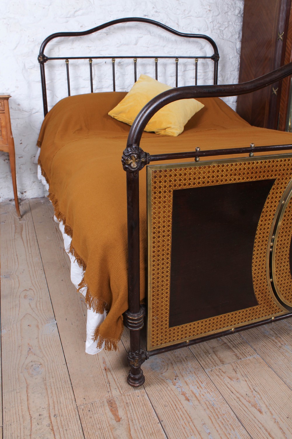 An antique European double bed featuring a dark iron frame, brass top rails, vertical spindles on the headboard, and decorative painted panel inserts on the footboard. View VIII