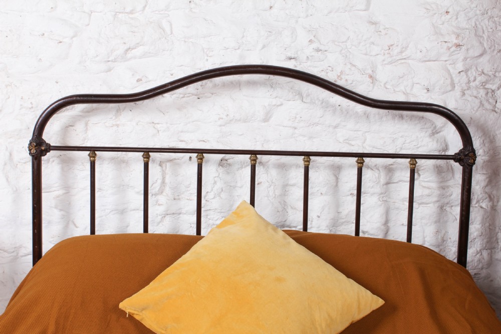 An antique European double bed featuring a dark iron frame, brass top rails, vertical spindles on the headboard, and decorative painted panel inserts on the footboard. View IX