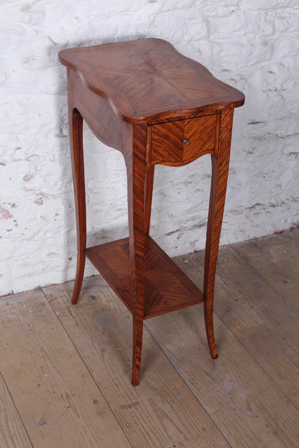 A tall French walnut veneer side table featuring a serpentine top with geometric parquetry inlay, a single front drawer, a lower tier shelf, and slender cabriole legs.