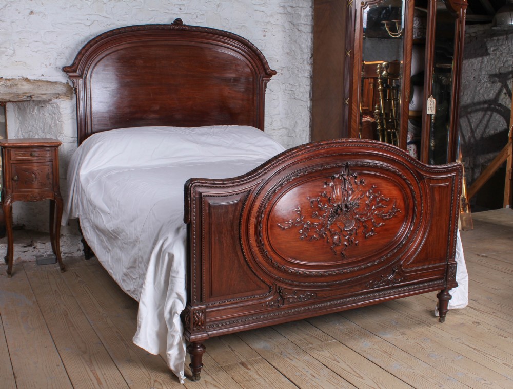 A French rosewood bed frame with a high arched headboard and a carved floral oval cartouche on the footboard.