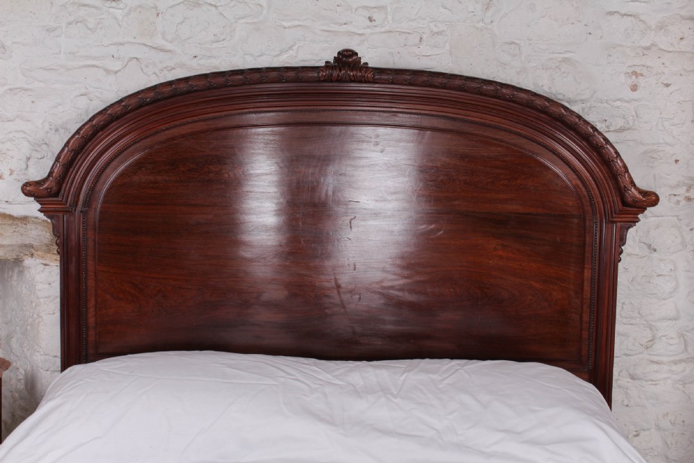 A French rosewood bed frame with a high arched headboard and a carved floral oval cartouche on the footboard. View III