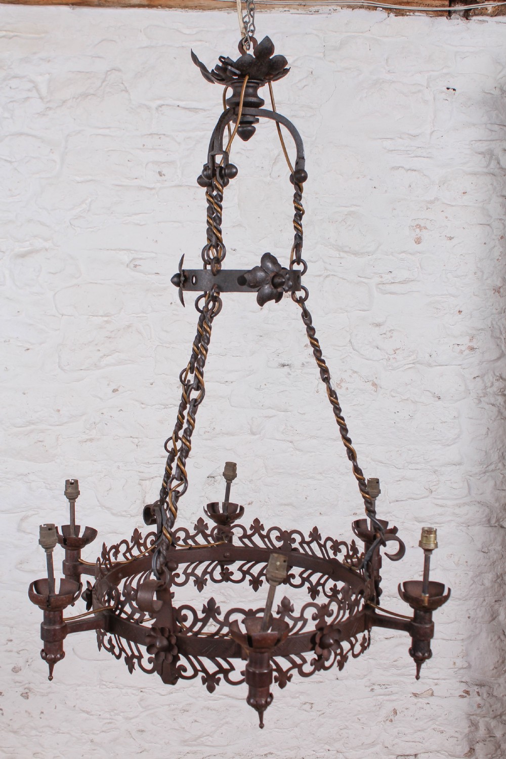 A French wrought iron chandelier with a pierced decorative rim, twisted iron support rods, and sculpted floral details.
