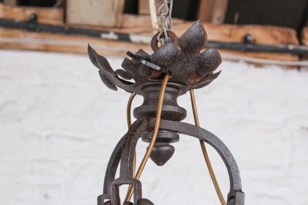 A French wrought iron chandelier with a pierced decorative rim, twisted iron support rods, and sculpted floral details. View V