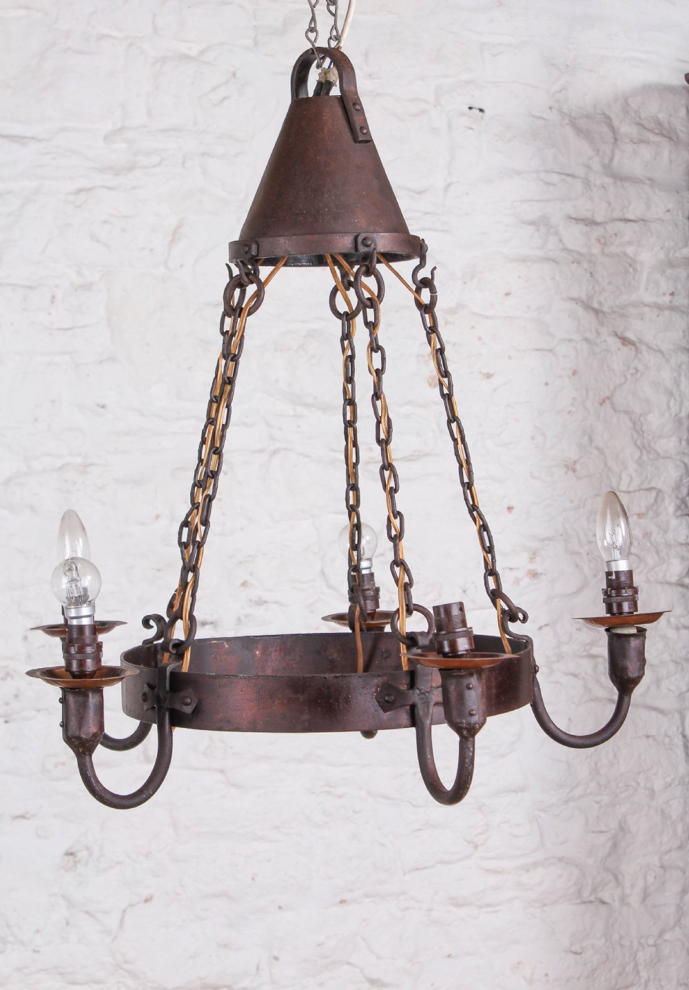 A patinated dark copper Arts and Crafts circular hoop chandelier suspended by four metal chains from a conical top cap.