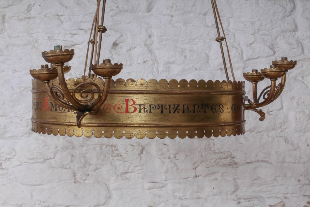 An Aesthetic Movement brass ecclesiastical corona chandelier featuring a circular band with painted Latin script, scalloped edges, multiple candle sconces, and hanging chains. View II