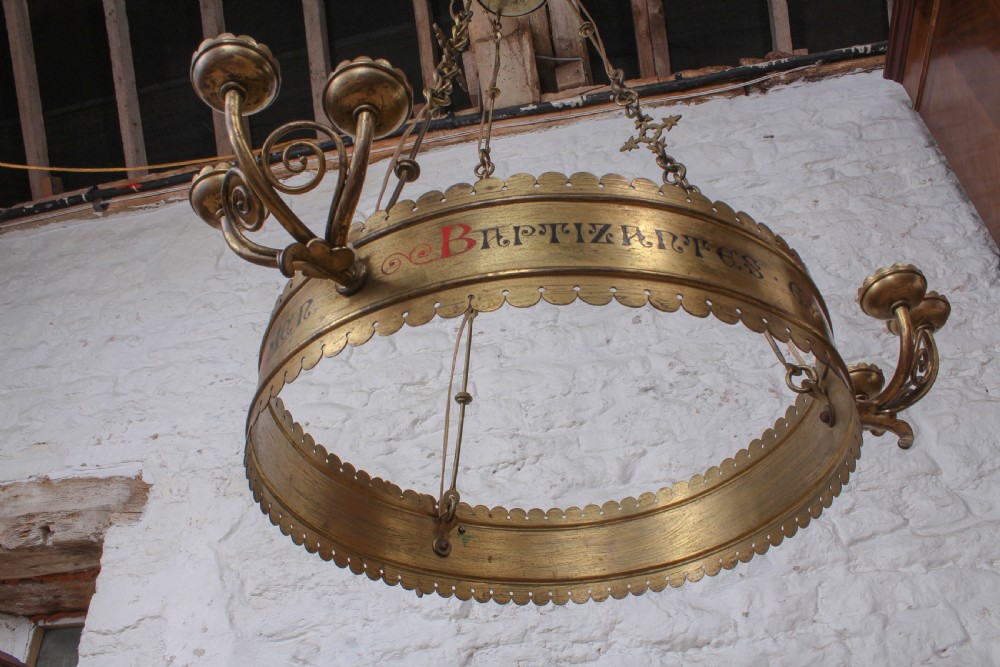 An Aesthetic Movement brass ecclesiastical corona chandelier featuring a circular band with painted Latin script, scalloped edges, multiple candle sconces, and hanging chains. View VI