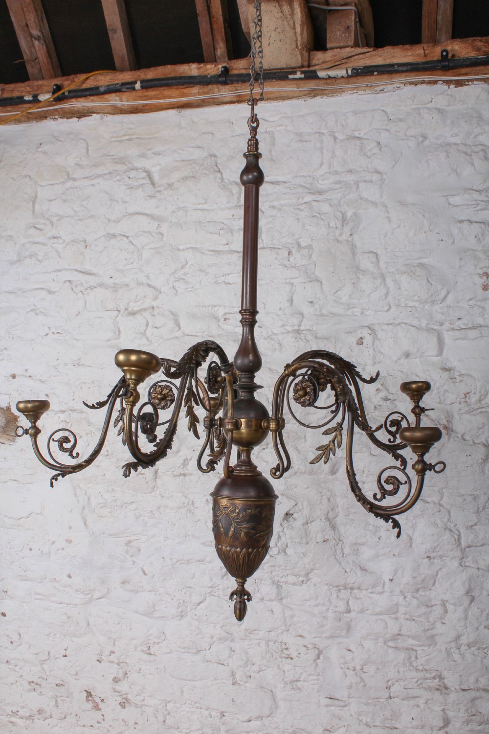 A French cast brass ceiling chandelier featuring scrolled arms, foliate leaves, floral rosettes, and a central turned stem with an urn-shaped lower finial.