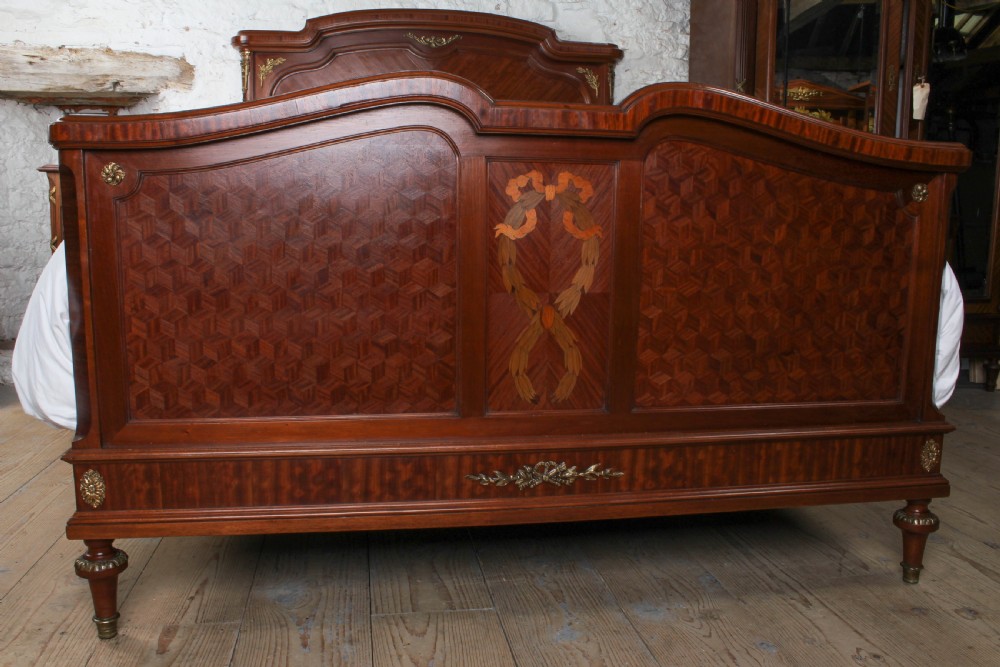 An antique French mahogany bed frame featuring geometric parquetry panels, fruitwood ribbon marquetry on the footboard, and gilt bronze mounts. View III